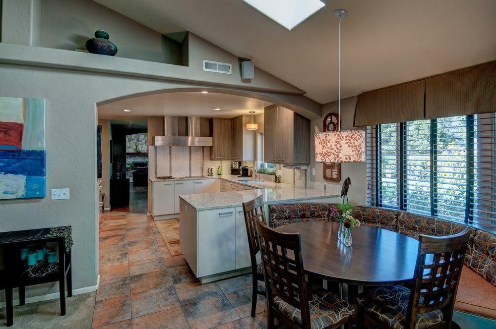 Open dining and kitchen area with tile floors, wood cabinets, round table, and large windows overlooking greenery