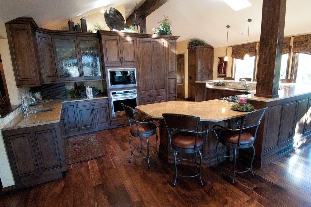 Warm kitchen with dark wood cabinets, hardwood floors, and a central round island with barstools.