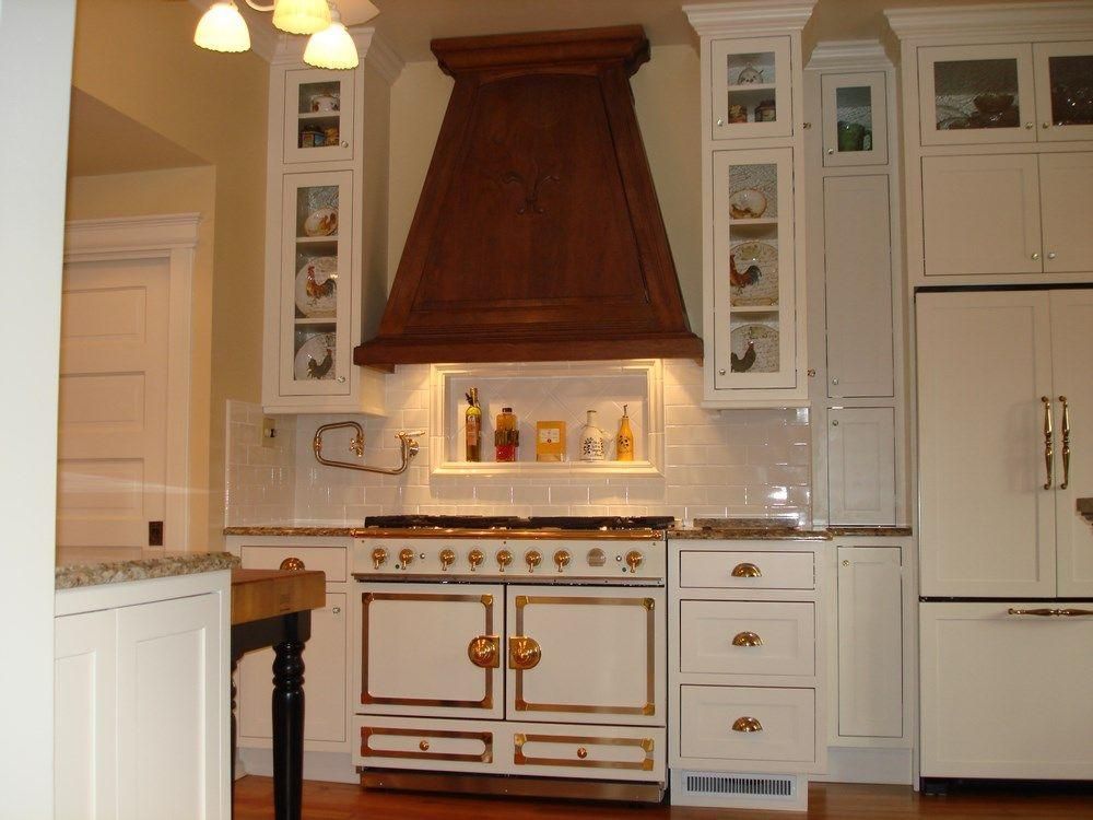 White kitchen with a large wooden range hood, marble backsplash, and built-in white cabinets.