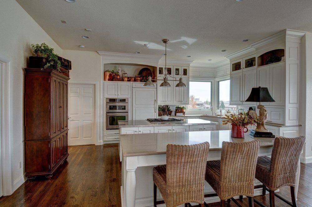 Bright white kitchen with island, wicker bar stools, wood cabinet, and large windows overlooking water.
