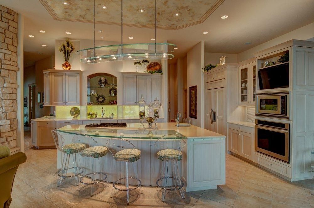 Bright luxury kitchen with a large island, bar stools, white cabinets, and built-in ovens