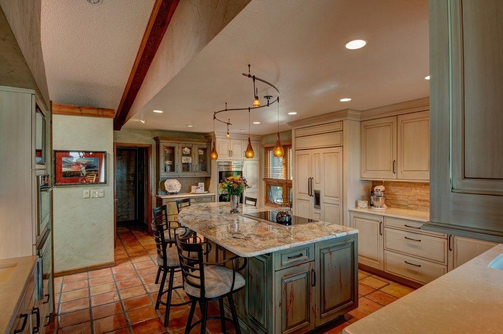 Bright kitchen with island, beige cabinets, and pendant lights; tiled floor and hallway view.