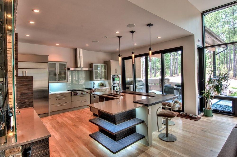 Modern open-concept kitchen and living area with wood floors, island seating, and large windows overlooking greenery