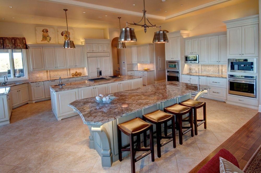 Bright modern kitchen with white cabinets, marble island, and five bar stools under pendant lights.
