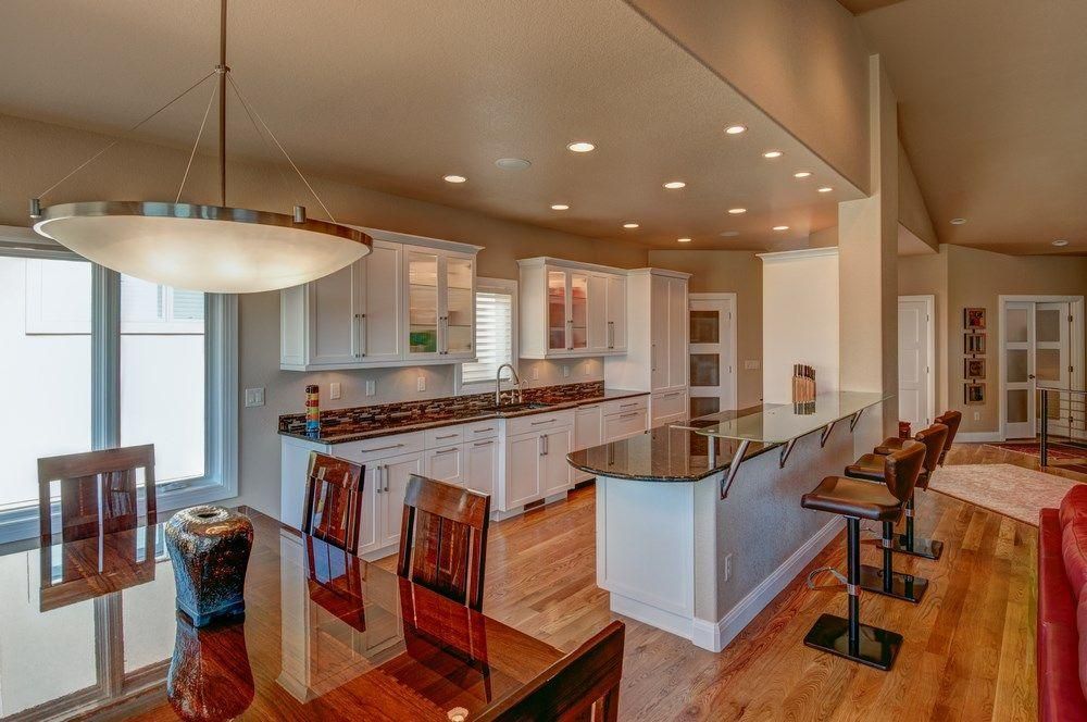 Bright open kitchen and dining area with white cabinets, dark countertops, and hardwood floors