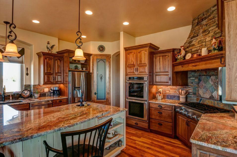 Warm kitchen with granite island, wood cabinets, stone fireplace, and stainless steel appliances
