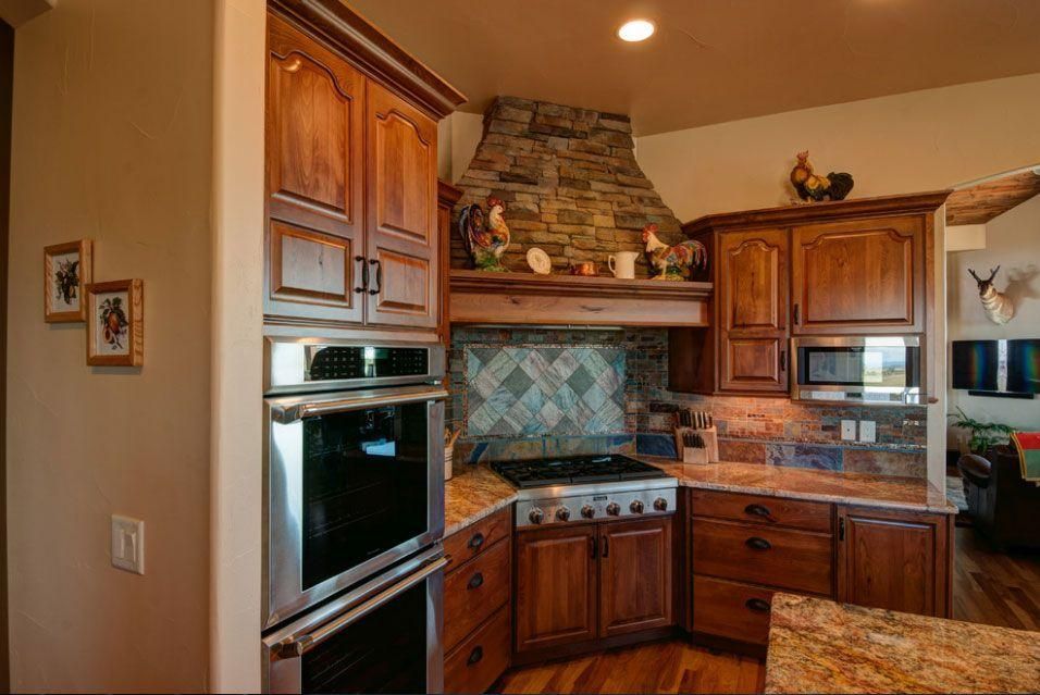 Warm kitchen with wood cabinets, stone range hood, stainless oven, and granite countertops