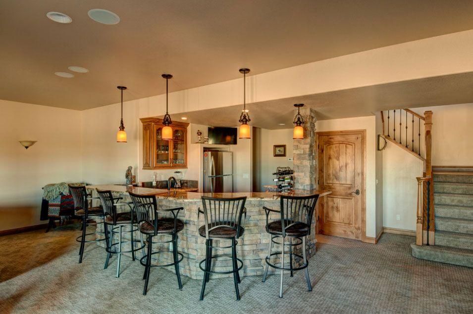 Open kitchen and bar with stools, pendant lights, and carpeted stairs in a warm-toned home interior