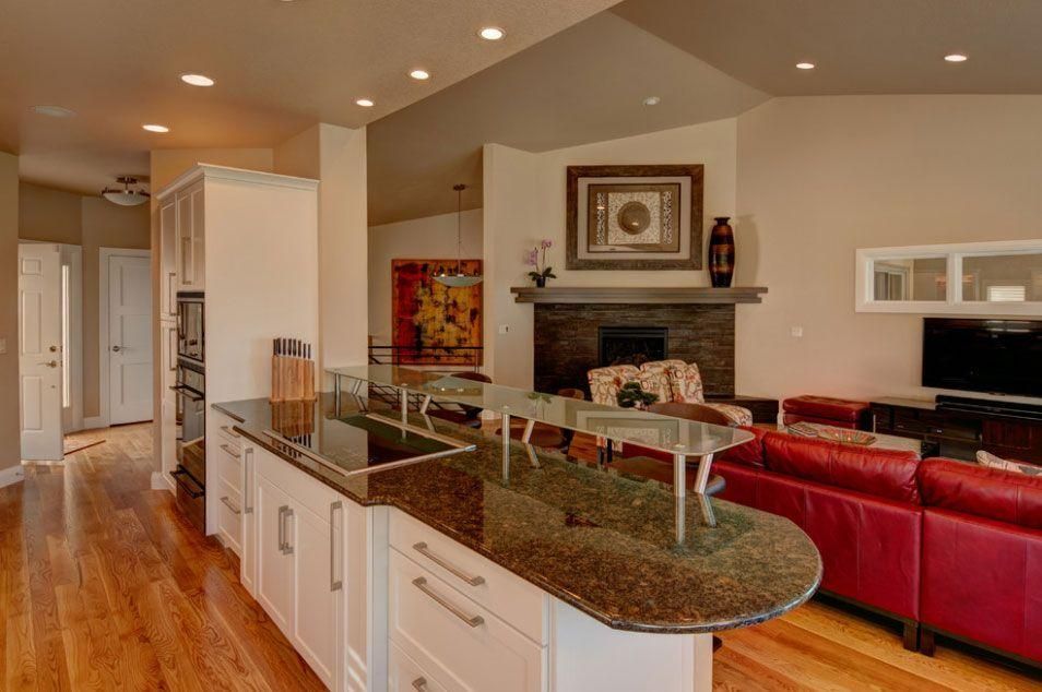 Open-concept kitchen and living room with granite island, red sofa, fireplace, and hardwood floors