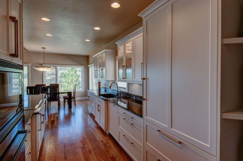 Long galley kitchen with white cabinets, wood floors, and sunlight from a window at the far end.