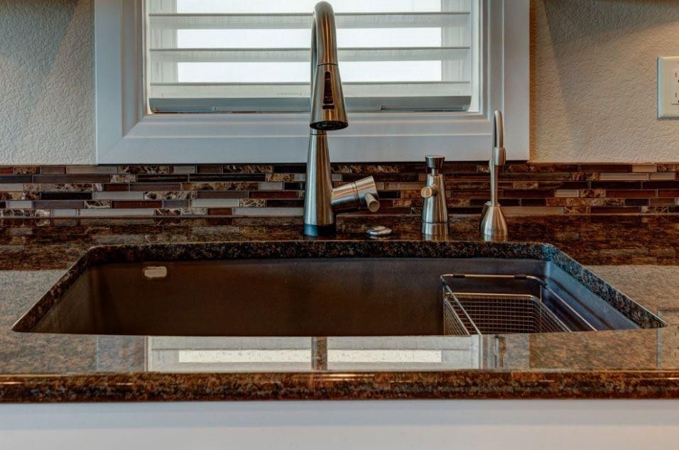 Modern kitchen sink with chrome faucet, brown granite countertop, and window above the basin