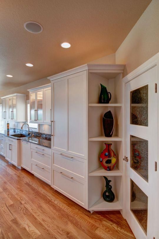 Bright, modern kitchen with white cabinets, hardwood floors, recessed lights, and a glass-front display cabinet.
