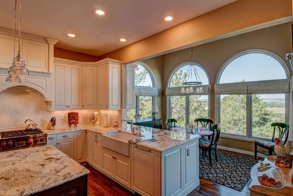 Bright, spacious kitchen with white cabinets, marble island, and large arched windows overlooking greenery