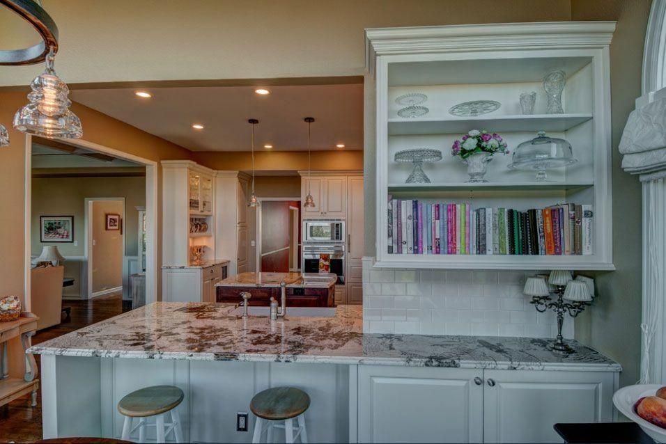 Bright kitchen with marble island, stools, white cabinetry, open shelving, and adjacent dining area