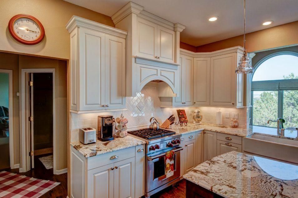 Elegant white kitchen with granite countertops, stainless stove, arched window, and warm recessed lighting.