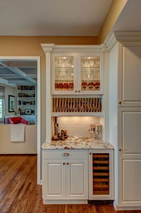 White built-in bar nook with glass cabinets, marble counter, and red-patterned wallpaper in a hallway