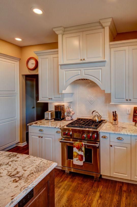 Bright kitchen with white cabinets, stainless range, marble backsplash, and wood floors