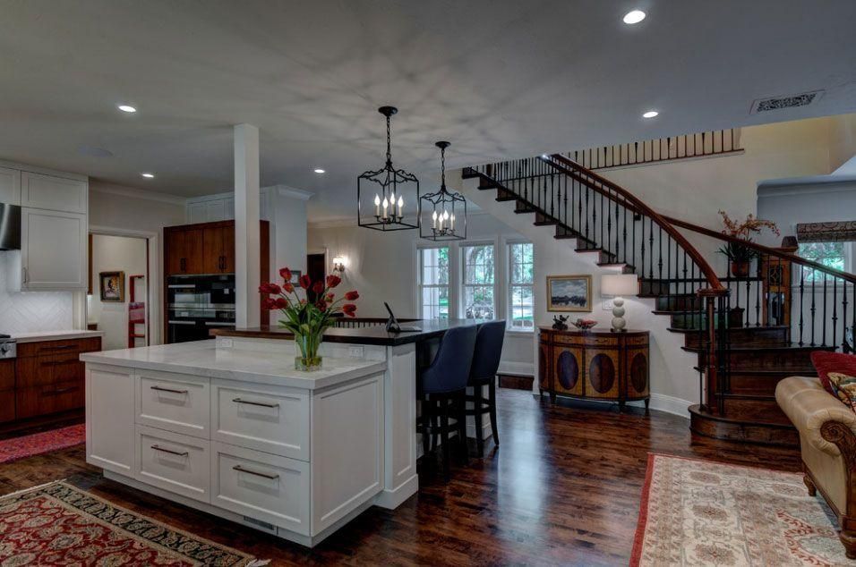 Modern open-concept kitchen and dining area with white island, dark chairs, hardwood floors, and staircase.