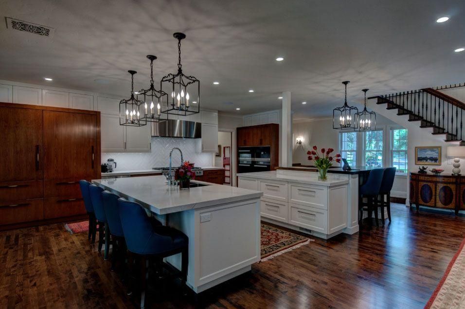 Open-concept kitchen with white island, dark cabinets, hanging chandeliers, and hardwood floors