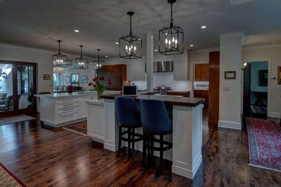 Open kitchen and dining area with dark wood floors, white cabinets, pendant lights, and blue bar stools