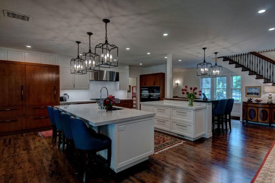 Open kitchen and dining area with white island, dark wood floors, pendant lights, and bar stools