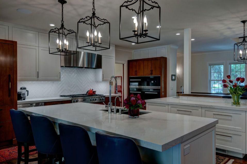 Modern kitchen with large marble island, blue chairs, pendant lights, and white cabinetry