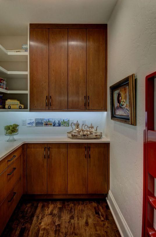 Small kitchen pantry with wooden cabinets, white countertop, and red shelving.