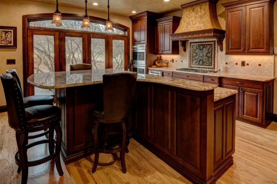Warm wood kitchen with island, granite counters, barstools, and hanging pendant lights.