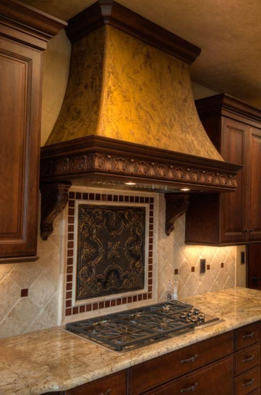 Kitchen stove with ornate bronze range hood, wooden cabinets, and beige tile backsplash