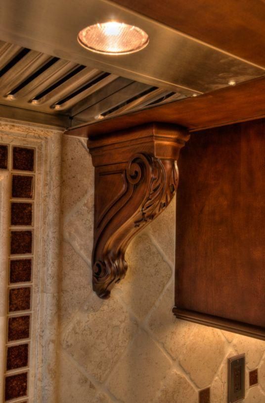 Decorative wooden corbel and stone backsplash under a stainless steel range hood with a light