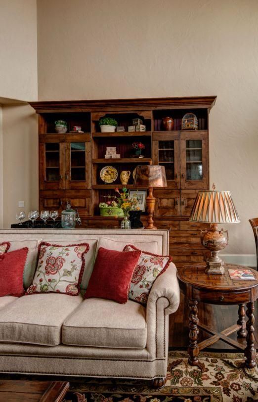 Cozy living room with beige sofa, red pillows, wooden hutch, patterned rug, and table lamp