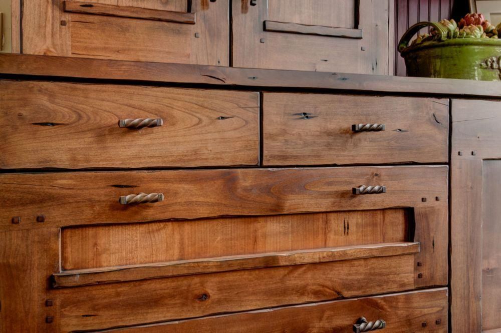 Wooden kitchen cabinet with drawers and a carved panel, in a rustic interior setting