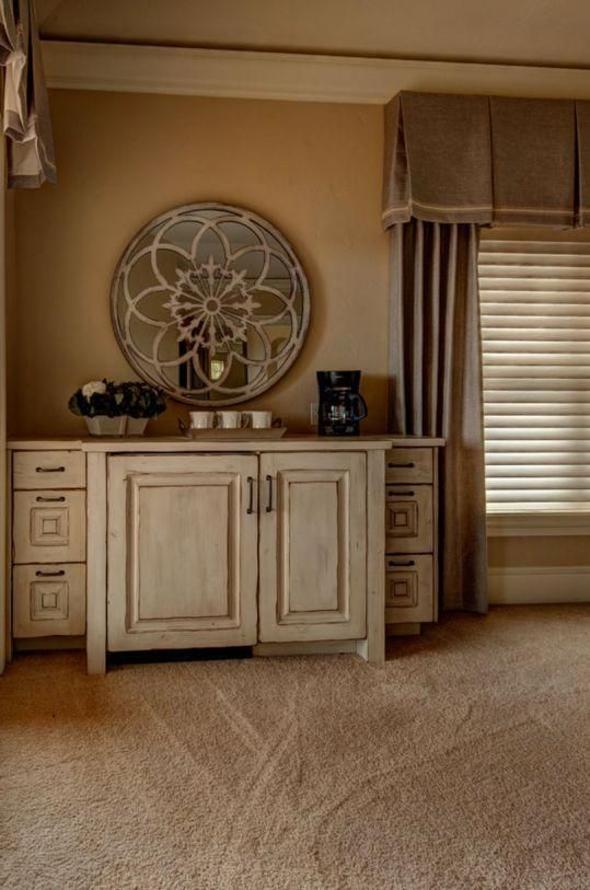 Beige bedroom with a white cabinet, decorative wall mirror, and window blinds.