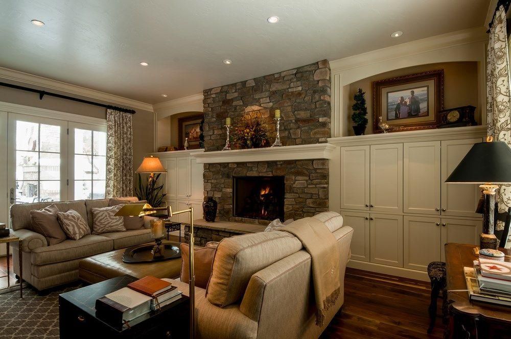 Cozy living room with stone fireplace, beige sofas, built-in cabinets, and warm recessed lighting.