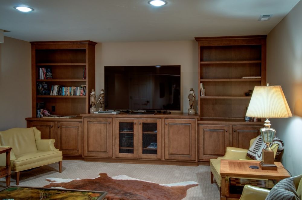 Living room with built-in wooden cabinets, a large TV, sofa, and lamp on a side table.
