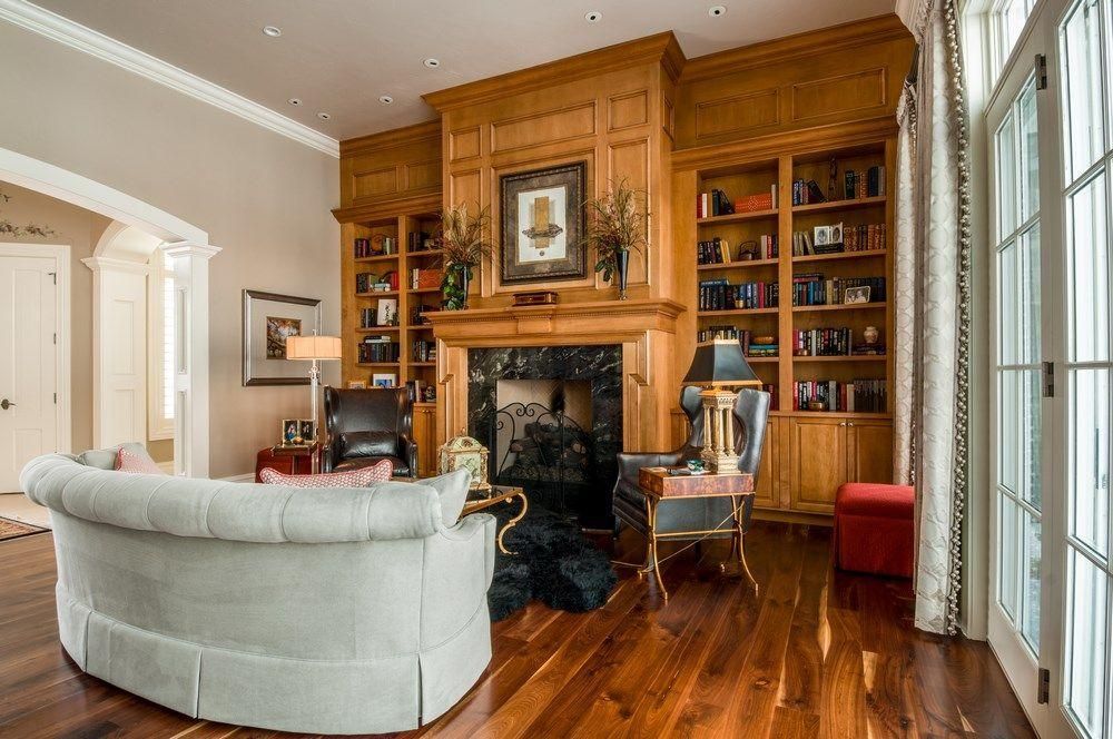 Elegant living room with wood-paneled walls, fireplace, built-in bookshelves, and a white sofa by tall windows