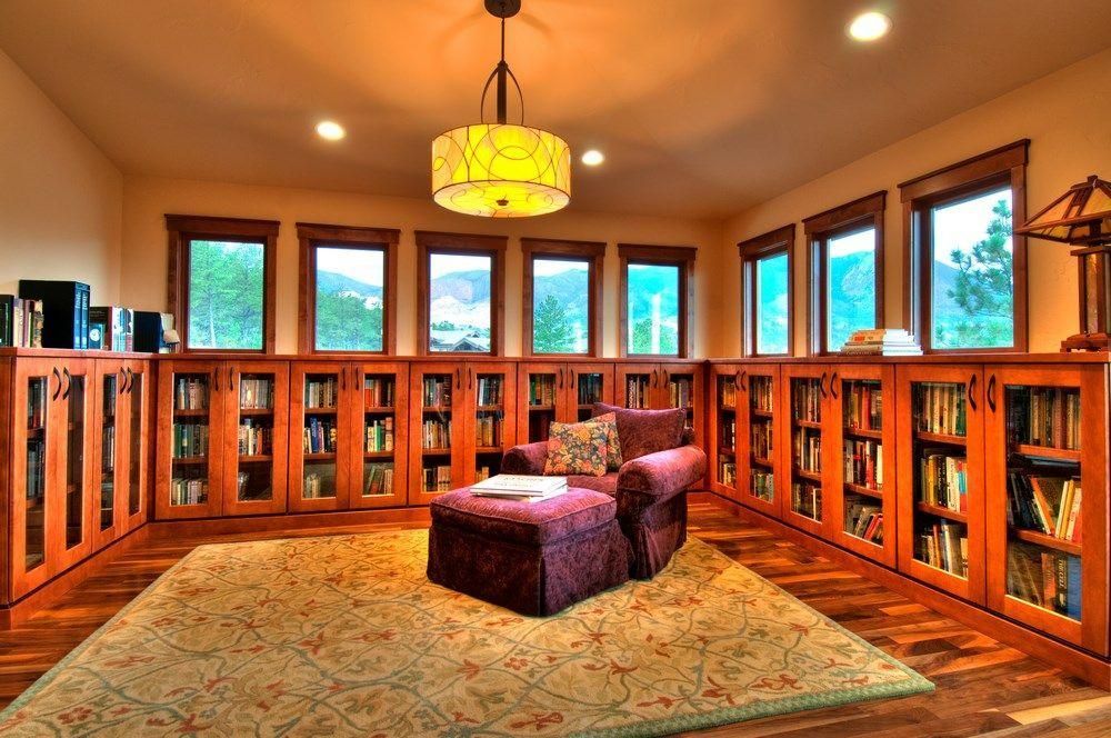 Cozy wood-paneled room with bookshelves, large windows, a rug, and two purple chairs under a hanging lamp
