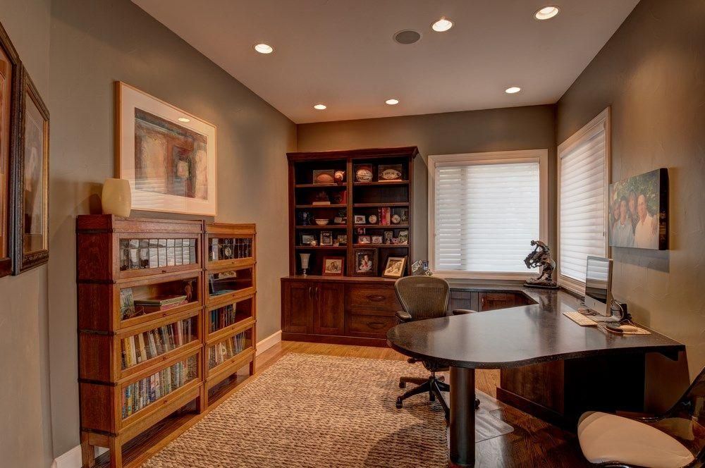 Home office with built-in bookcases, a desk, and warm recessed lighting