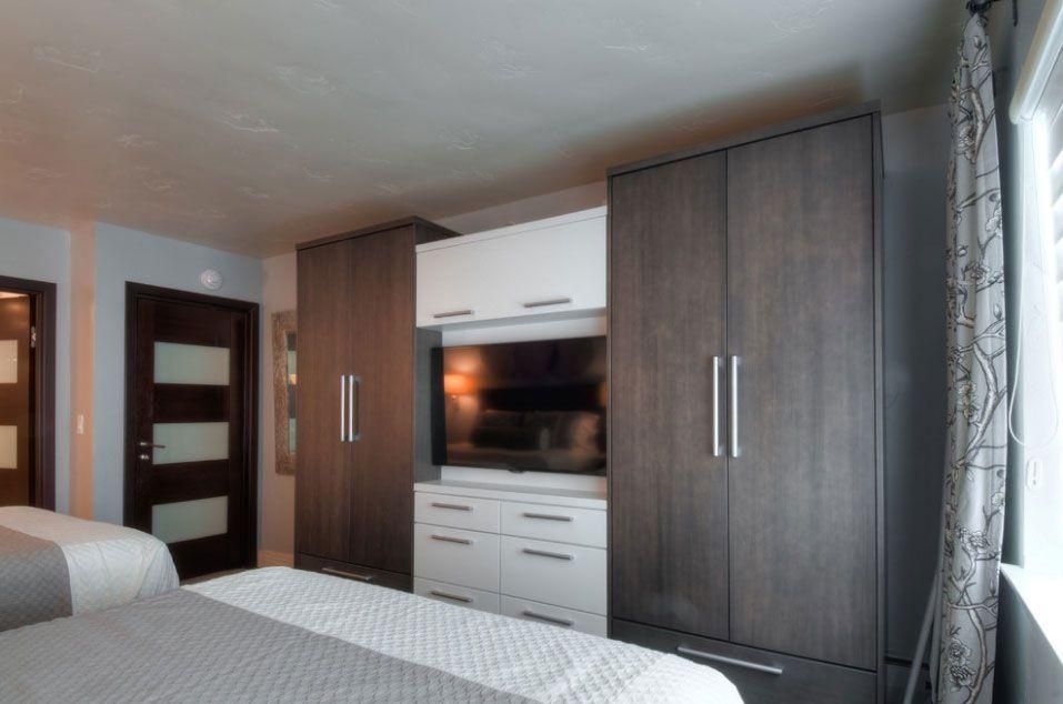 Hotel room with two beds, dark wood wardrobes, TV, and large window with curtains
