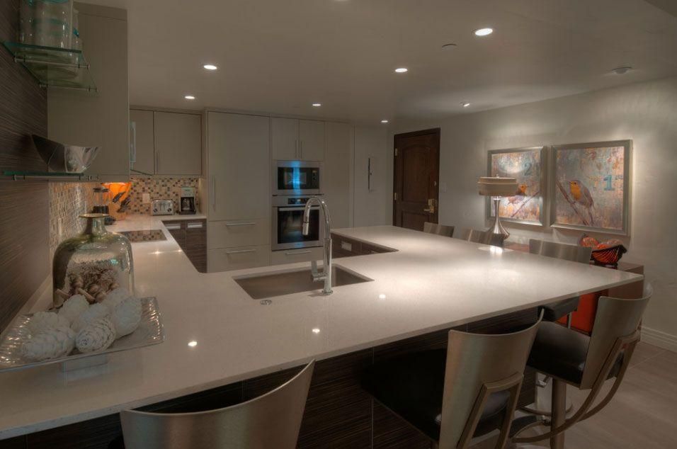 Modern kitchen with a large white island, built-in appliances, and bar stools under recessed lighting
