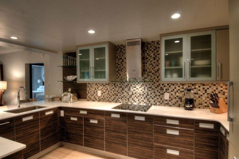 Modern kitchen with brown cabinets, mosaic backsplash, white counters, and glass-front upper cabinets