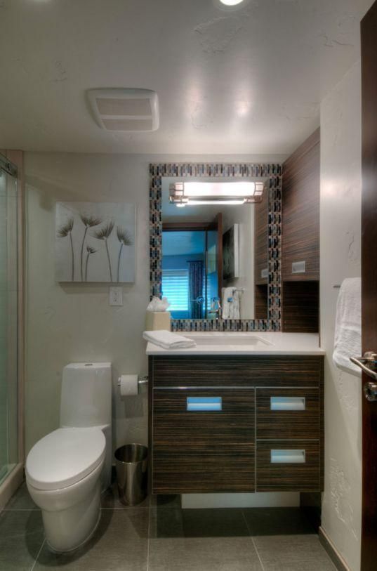 Modern bathroom with toilet, vanity sink, mirror, and white walls with dark wood cabinets.