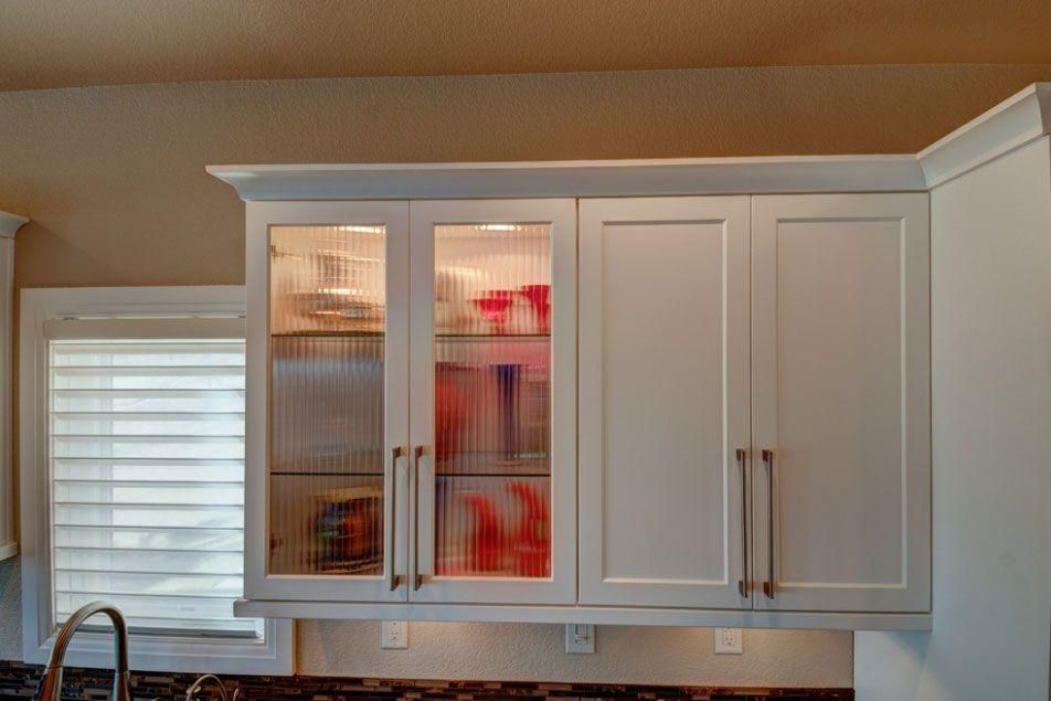 Kitchen wall cabinets with white doors and glass panels, lit from inside, above a window and countertop