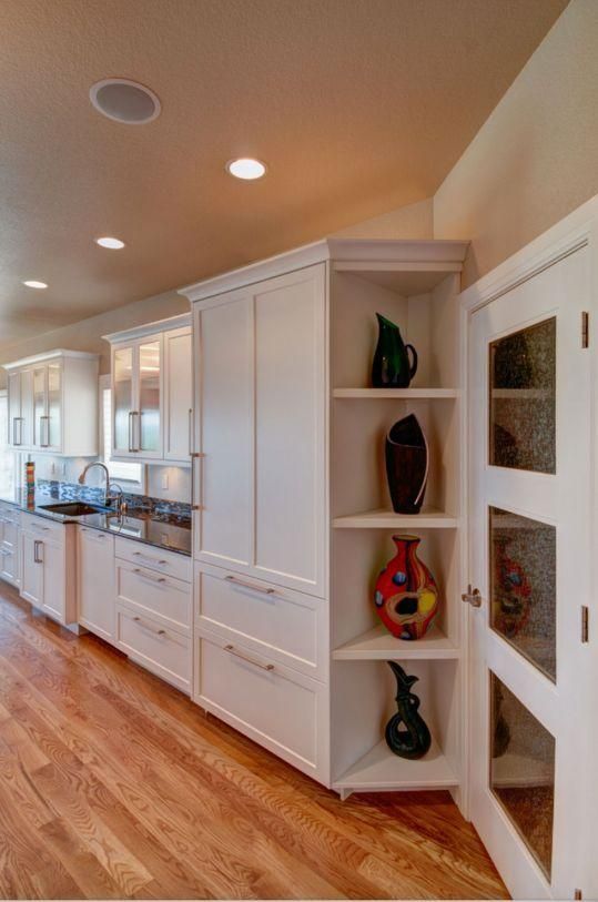 Bright kitchen hallway with white cabinets, hardwood floors, and built-in display shelves with vases.