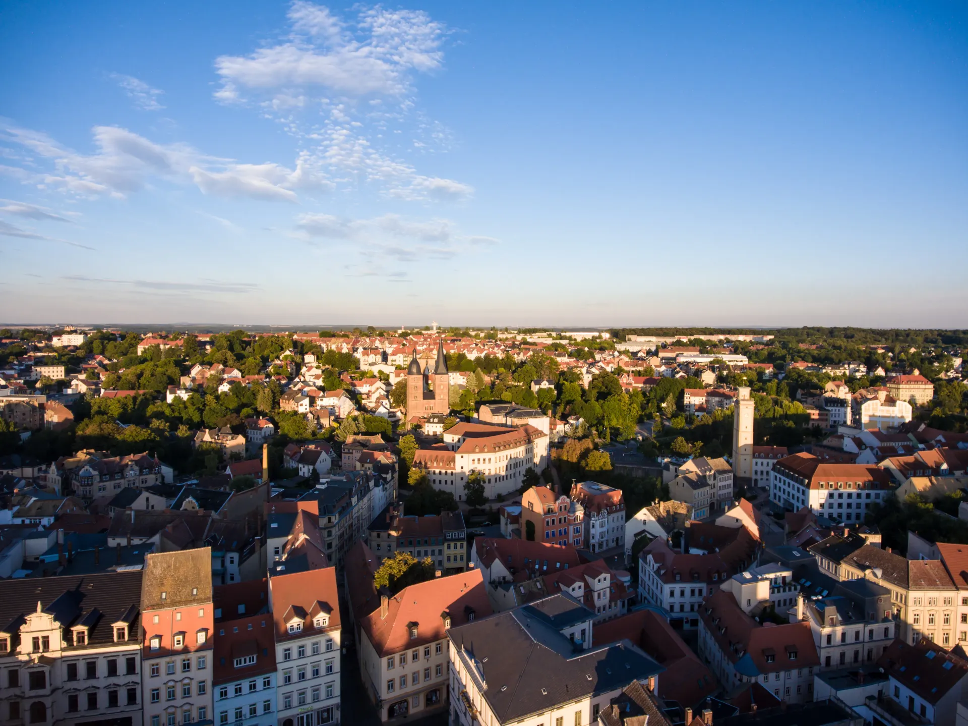 Aerial view of a European town with red-tiled roofs, buildings, trees, and a clear blue sky.