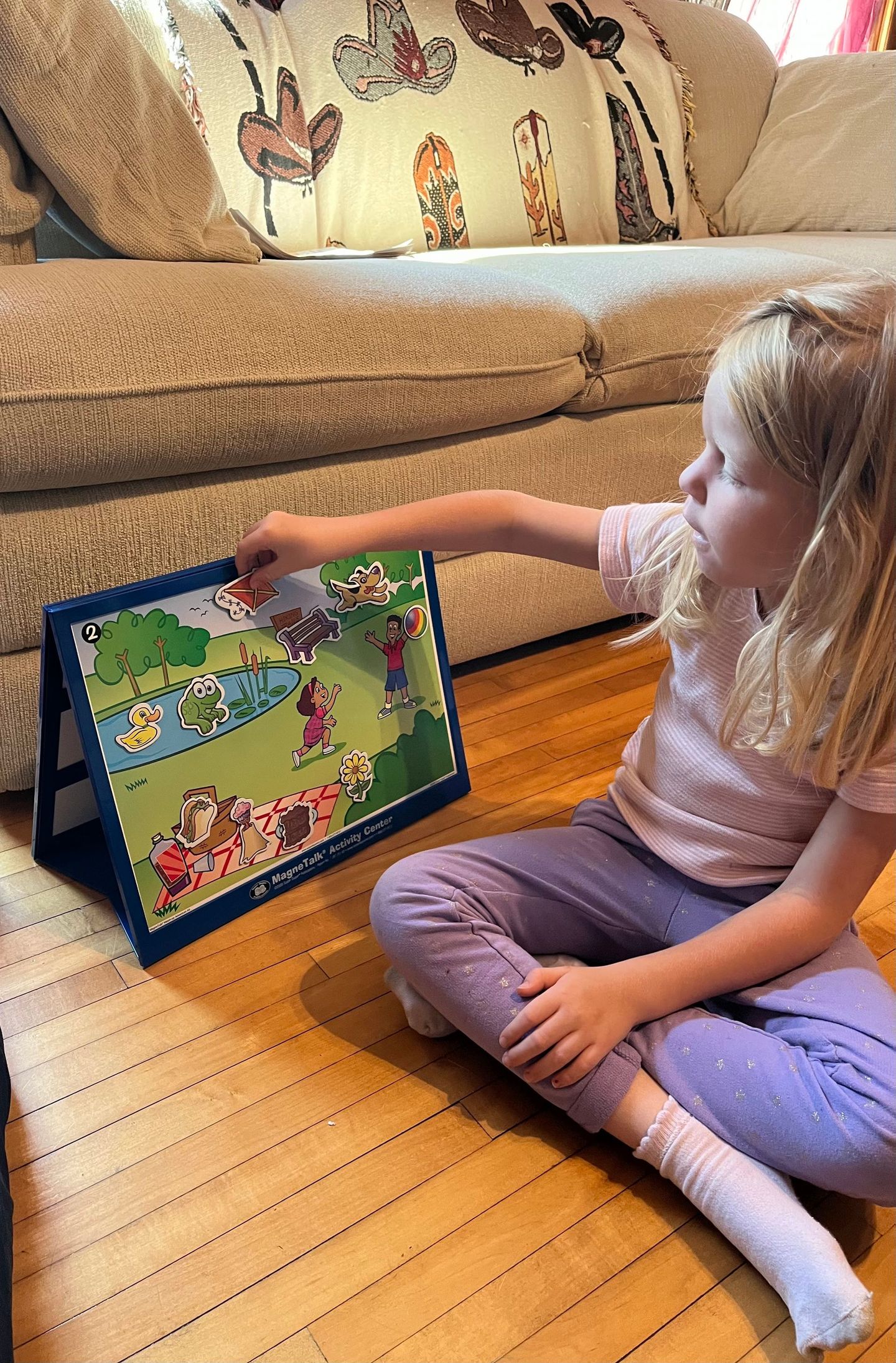A little girl is sitting on the floor playing with a magnetic board.