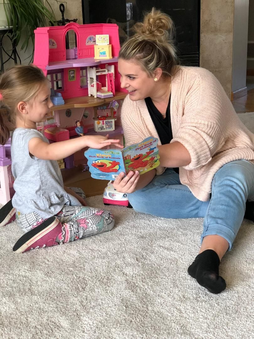 A woman is sitting on the floor reading a book to a little girl.