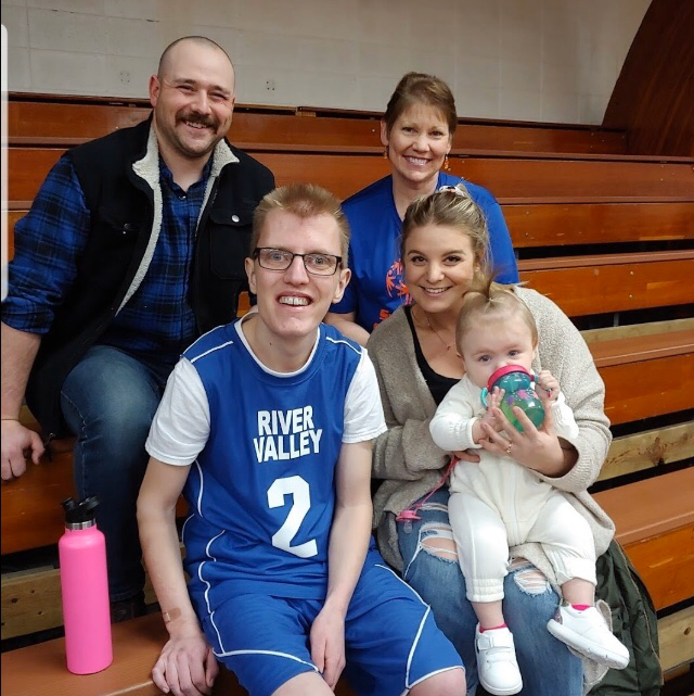 A man wearing a river valley jersey is holding a baby