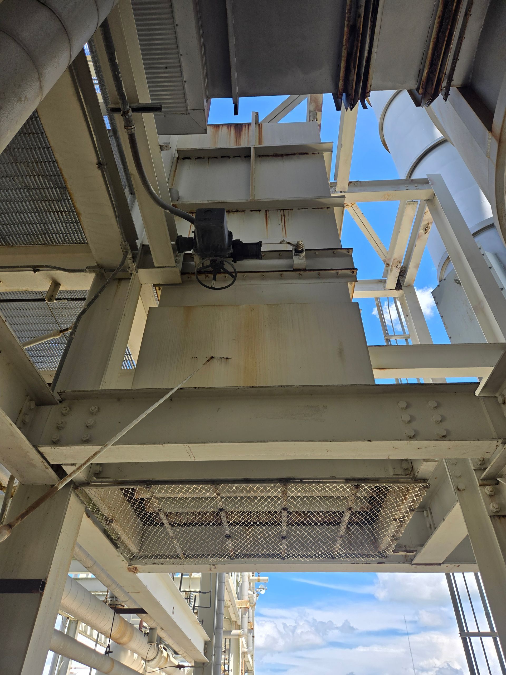 Industrial steel structure and machinery inside a building, with blue sky visible through the open framework.