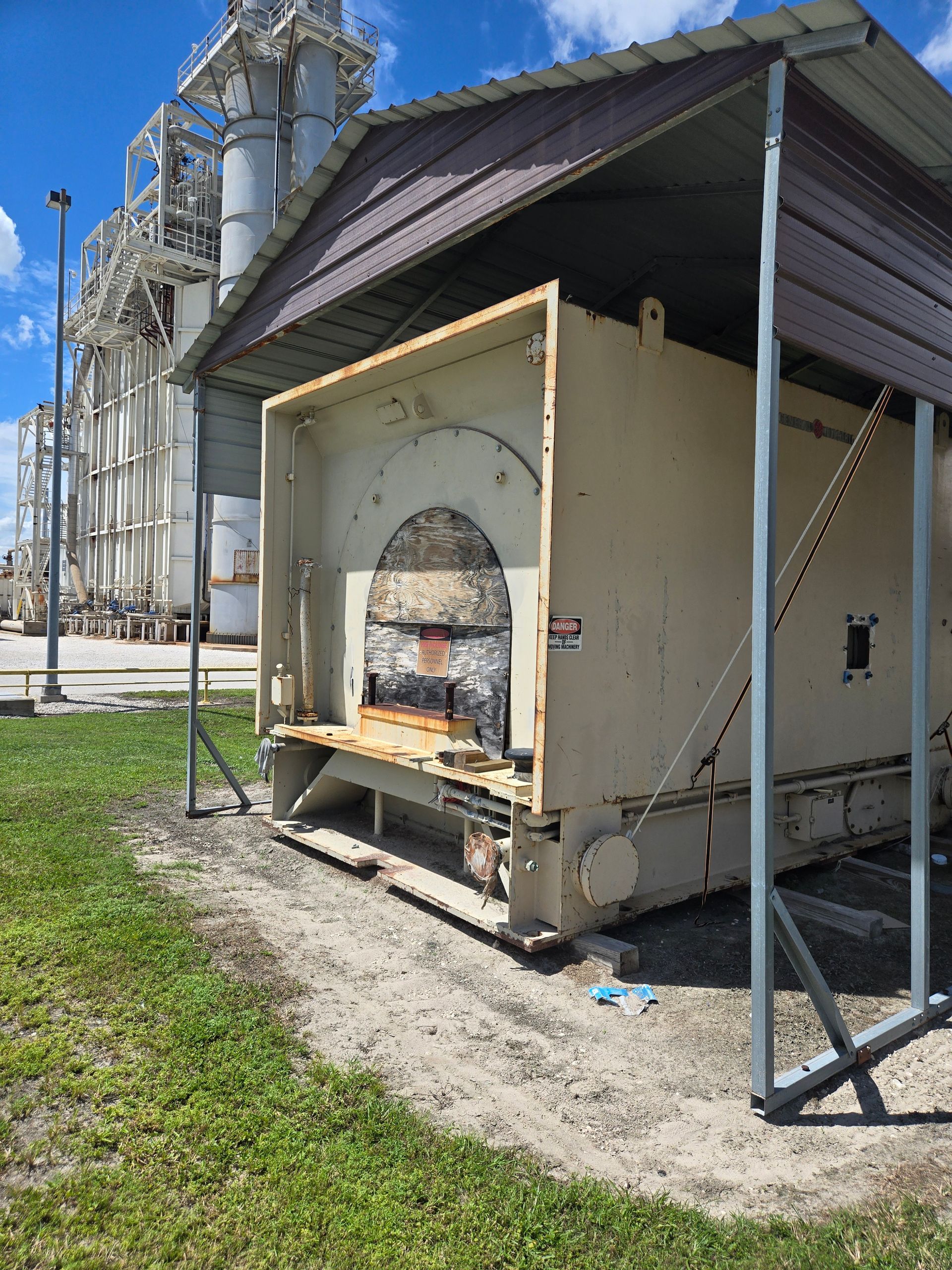 Portable kiln or oven in a metal shelter beside an industrial building on a grassy lot